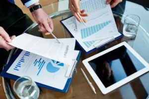 Business professionals reviewing a signed contract and financial data charts on a glass table during a procurement strategy meeting.